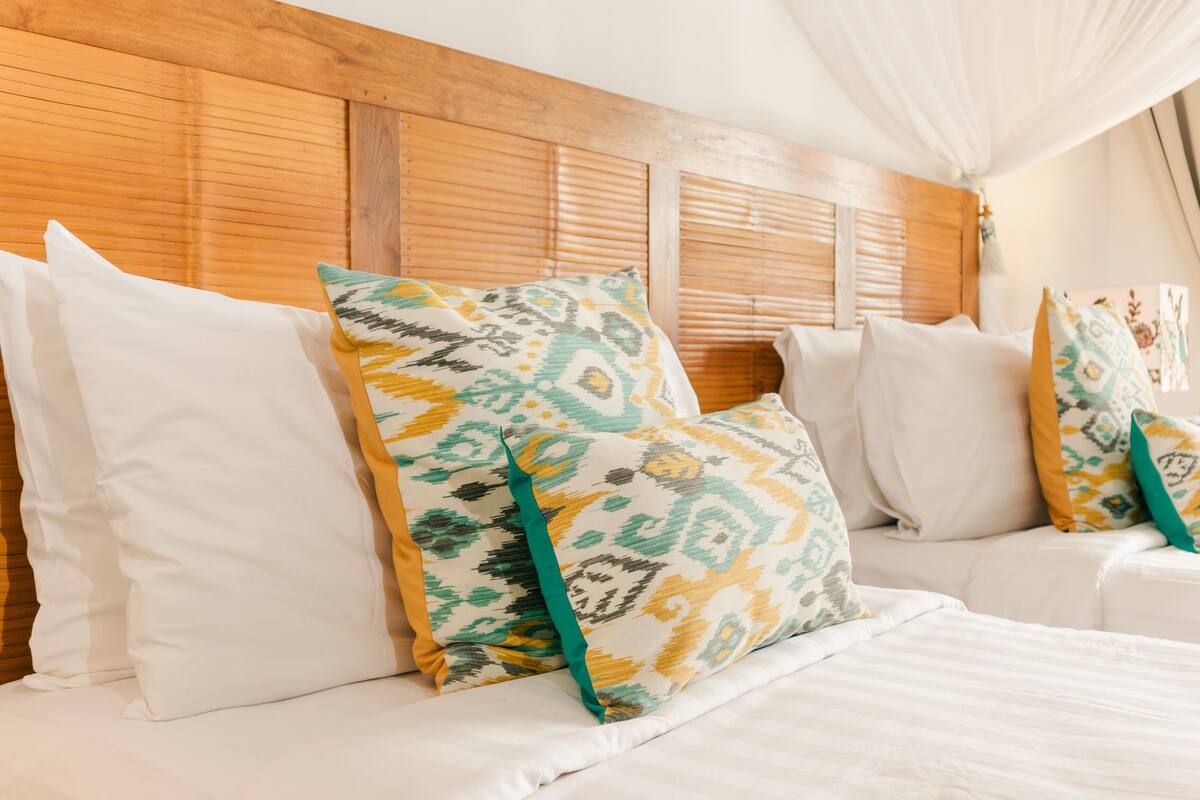 A hotel room with a wooden headboard, white bedding, and patterned throw pillows.