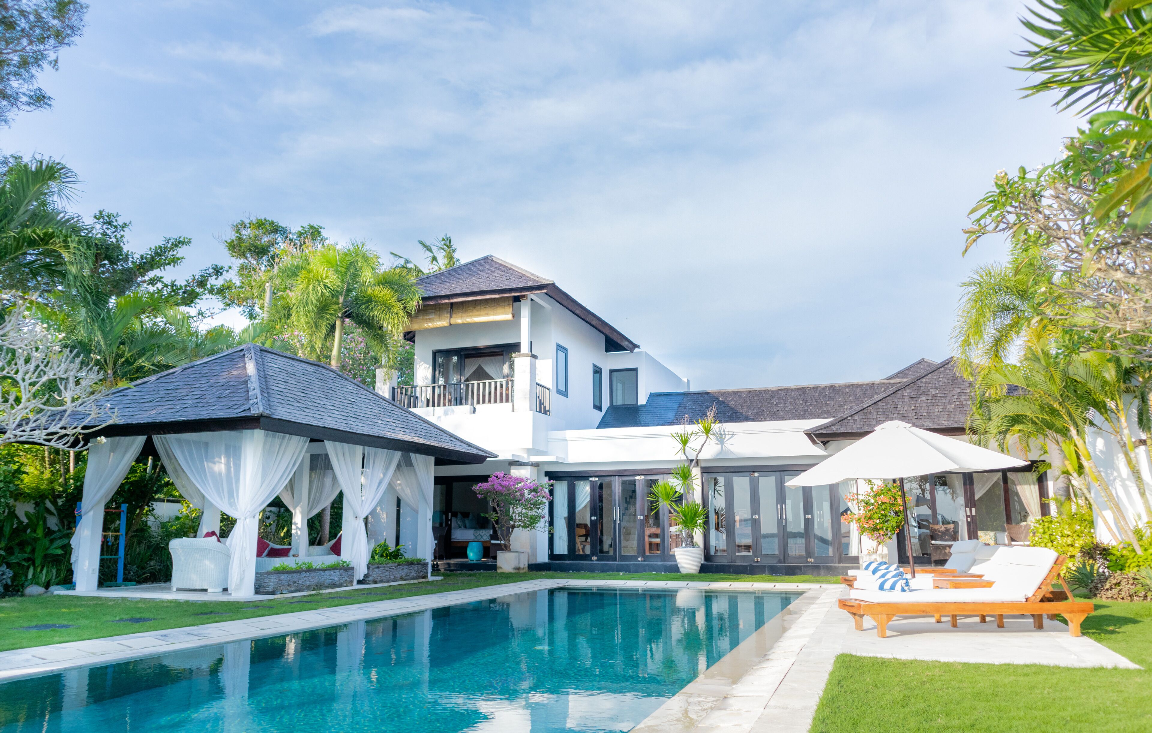 Una casa de dos pisos con piscina, un pabellón y mobiliario exterior.