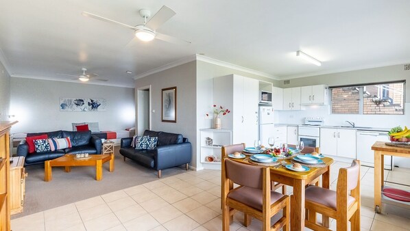 Un salon moderne avec un canapé, une table basse et un coin repas comprenant des chaises et une table dressée pour un repas.