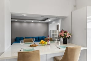 A modern dining area with a white table, blue and beige chairs, a fruit bowl, wine glasses, and a vase of flowers.