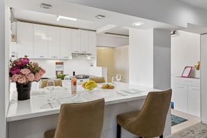 A modern kitchen with white cabinets, a central island with seating, and a dining area.
