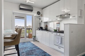 A modern kitchen with white cabinets, a stove, and a large window overlooking a cityscape.