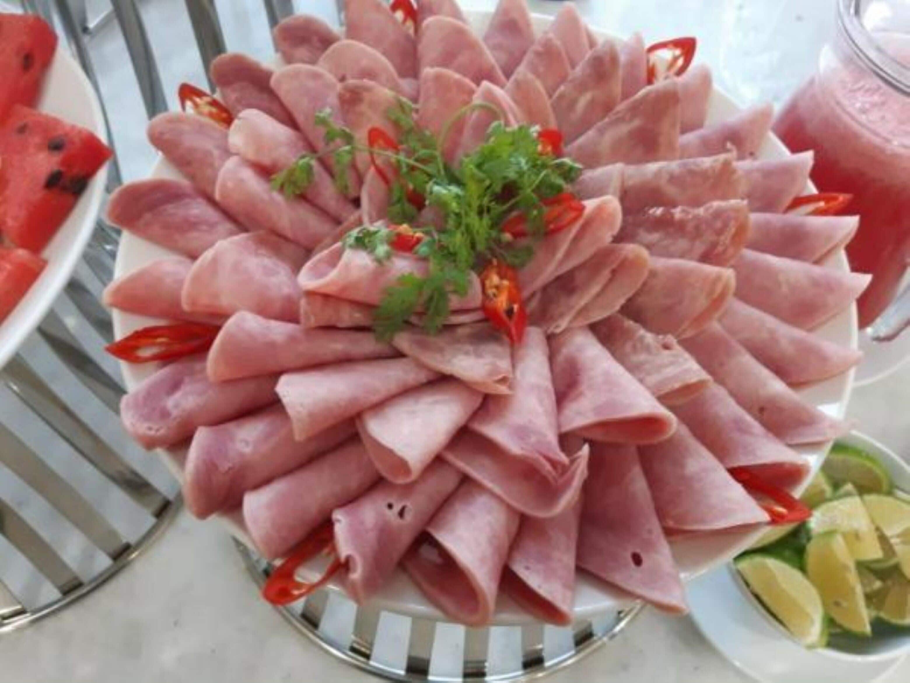 Une assiette de fines tranches de viande disposées en cercle, garnie d’herbes aromatiques et de piments.