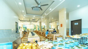 Disposição de buffet com várias estações de comida, um ventilador de teto e um sinal indicando o banheiro.
