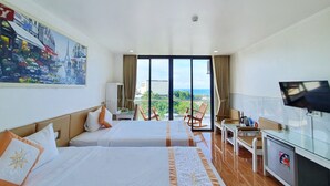Quarto de hotel com duas camas, televisão, escrivaninha e vista para o mar.
