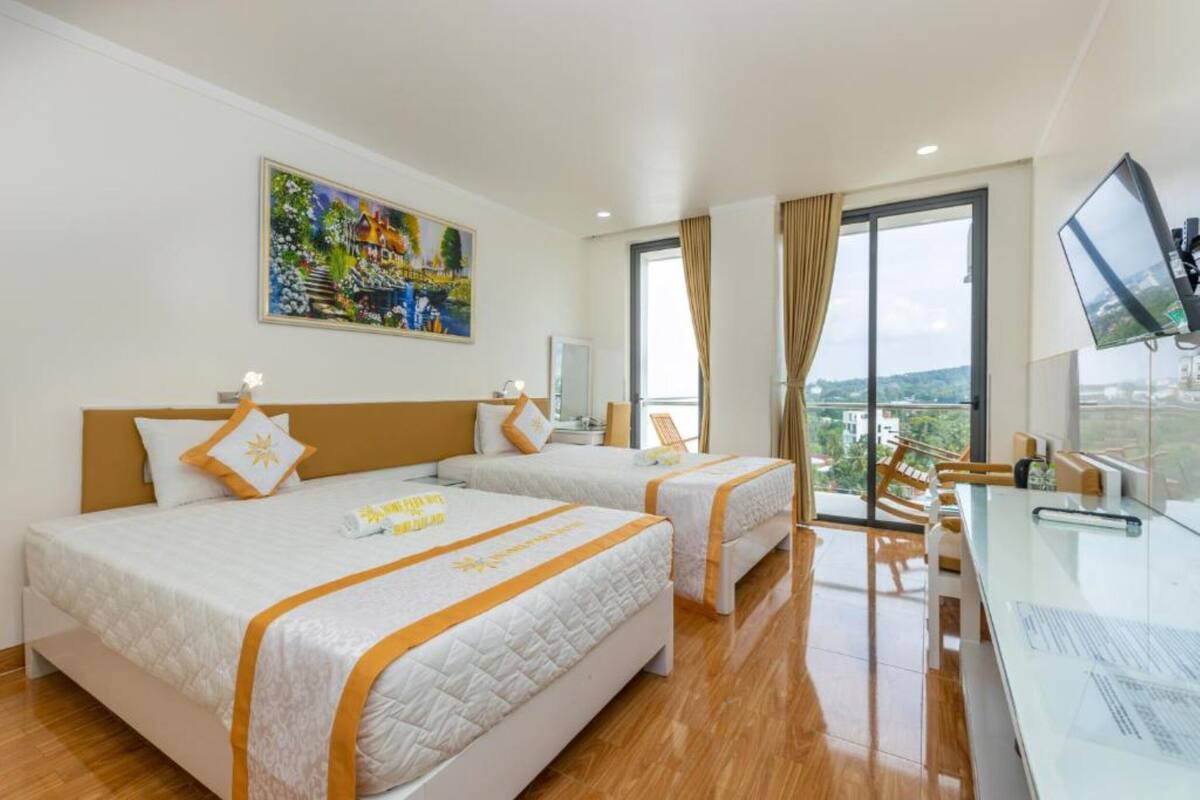 A hotel room with two beds, a desk, a TV, and a large window with a city view.