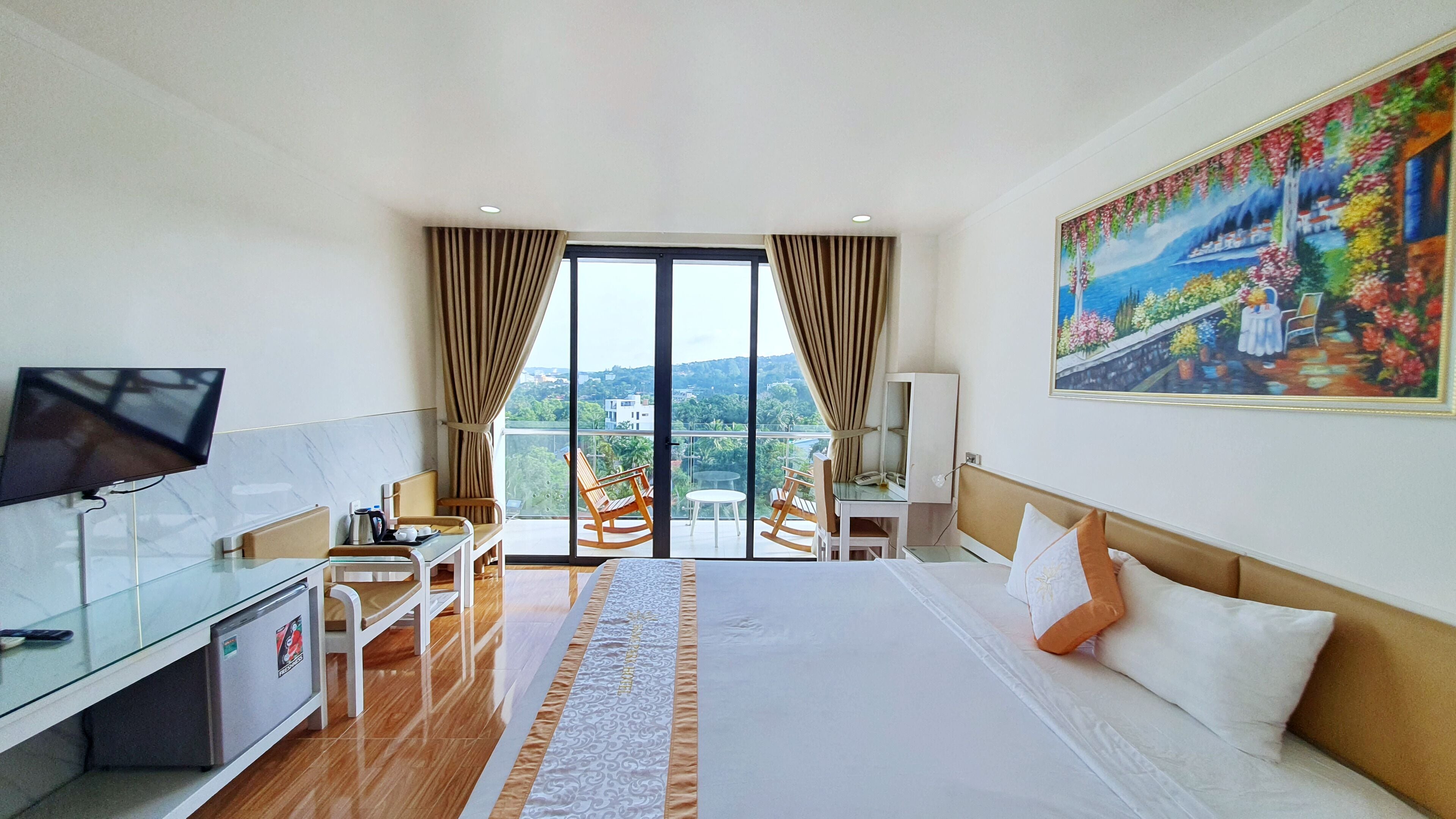 Habitación de hotel con una cama grande, un escritorio con una computadora, un televisor y un balcón con vista a la ciudad.