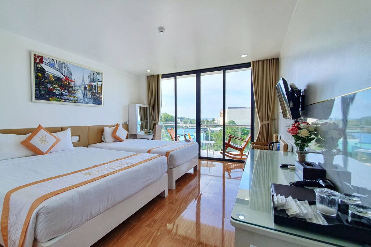 A hotel room with two beds, a large painting, a balcony with a view, and a desk with amenities.