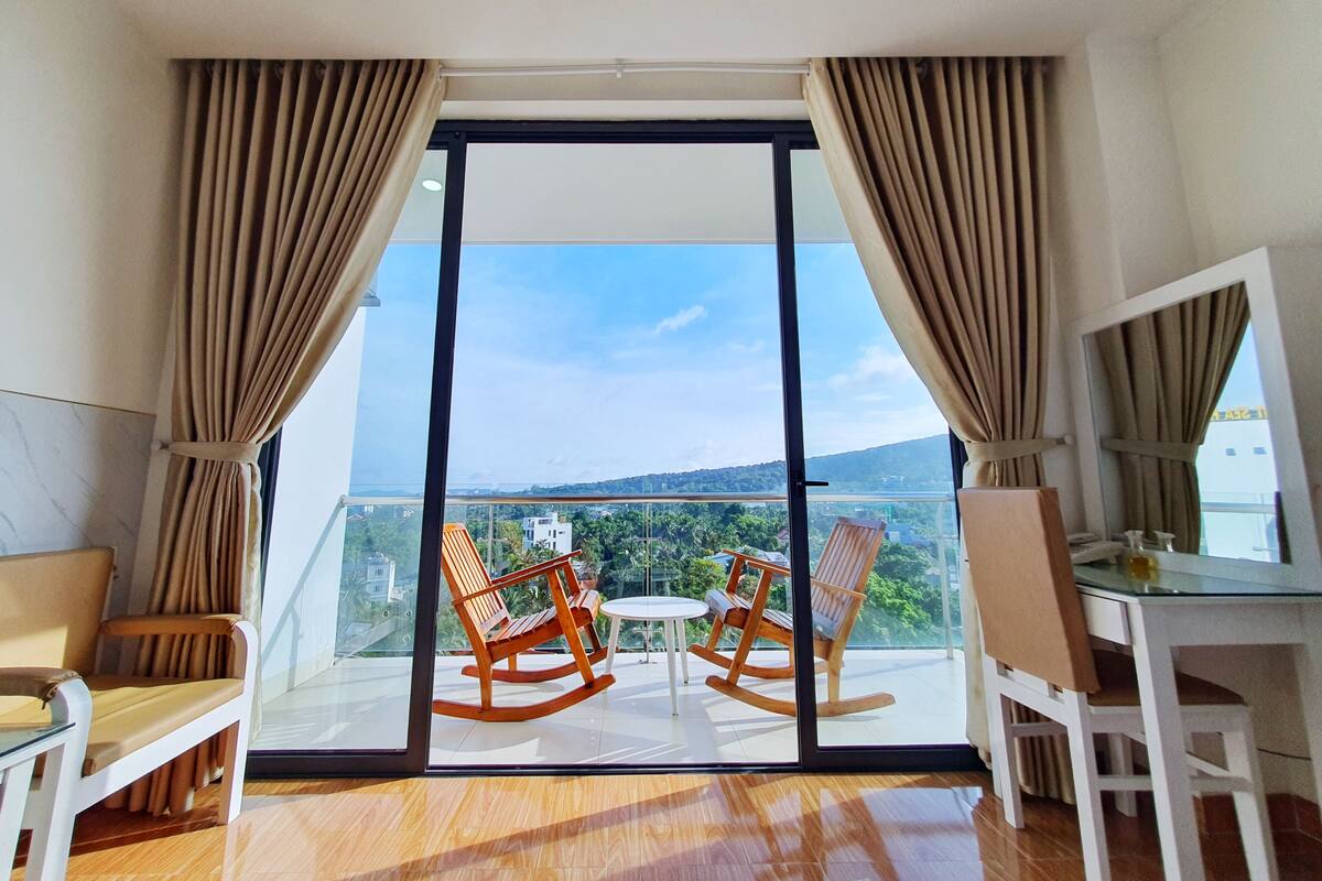 A balcony with two rocking chairs and a small table, overlooking a scenic view.