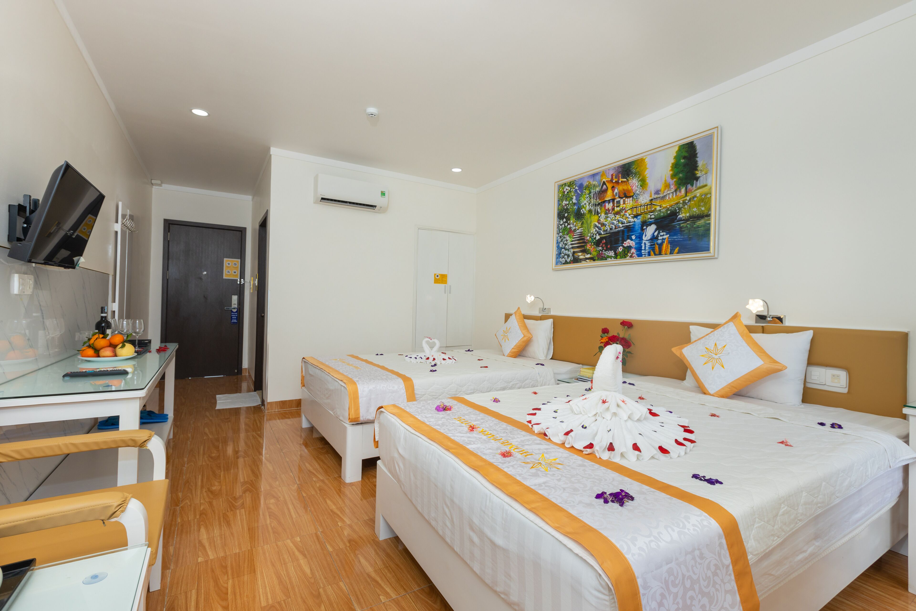 A hotel room with two beds, a desk with a computer and a chair, a TV, and a painting on the wall.