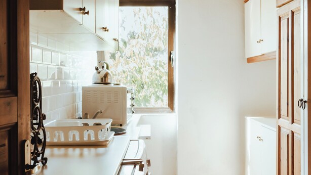 A kitchen with wooden ceiling beams, white cabinets, and a window with a view of trees. - Amnisiades Apartments (Heraklion)