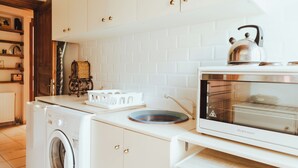 A kitchen with a washing machine, a microwave, and a kettle on the counter. - Amnisiades Apartments (Heraklion)