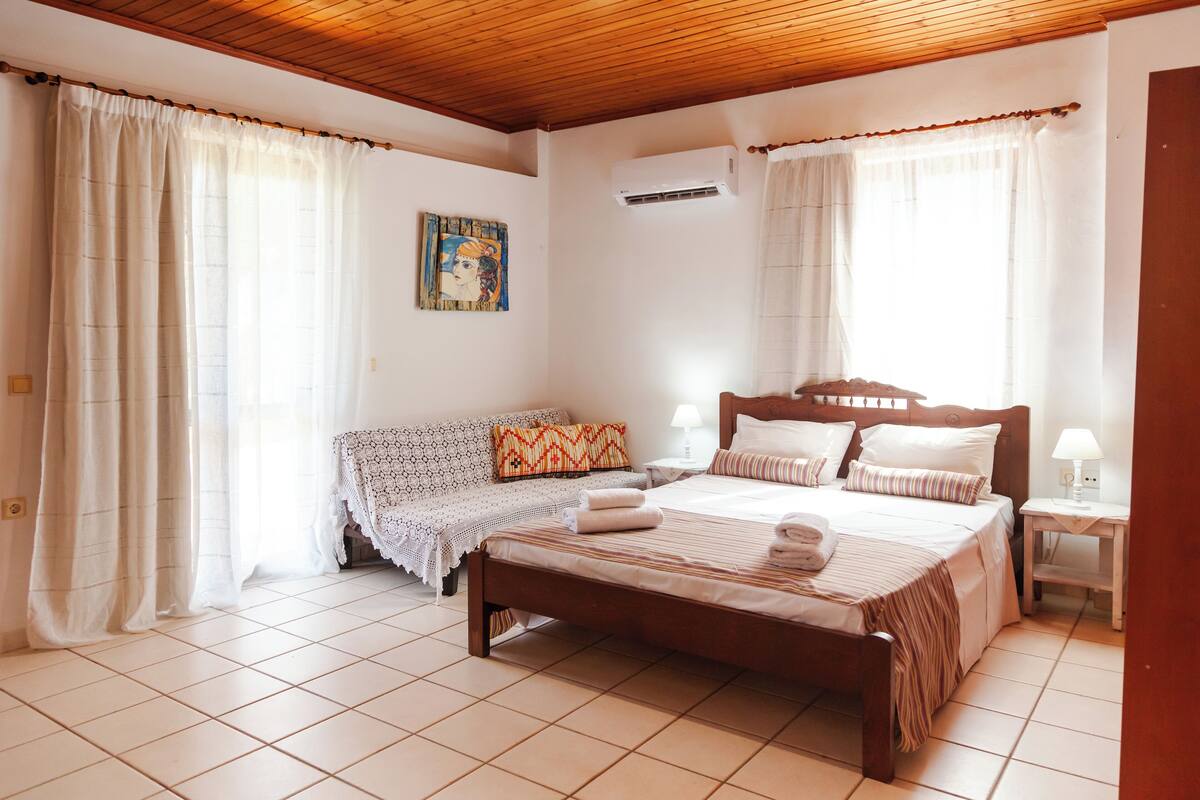 Quarto com cama de madeira, um sofá e uma mesinha de cabeceira.