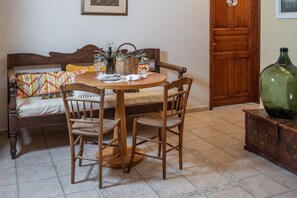 A dining area with a round wooden table, two chairs, a wicker basket, a bottle, and a green vase on a cabinet.