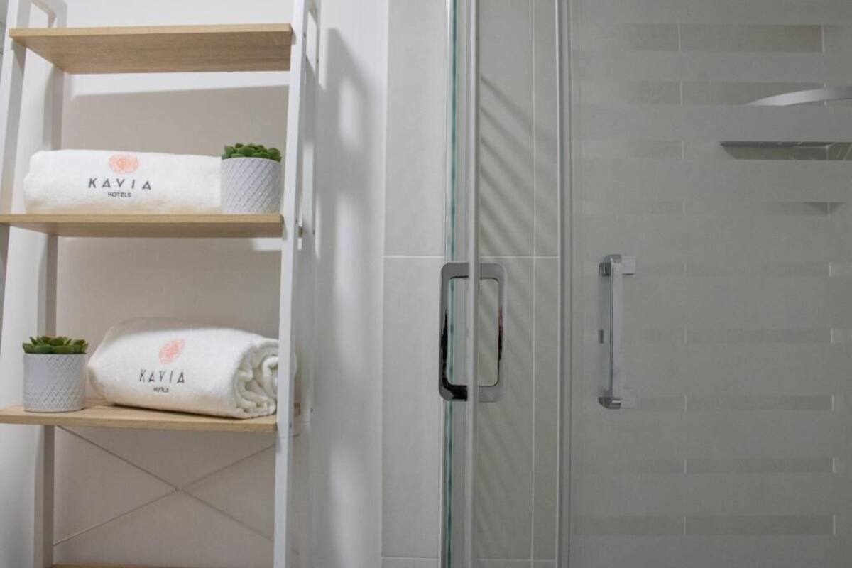 A bathroom with a glass shower door, a towel rack with towels, and a small potted plant.