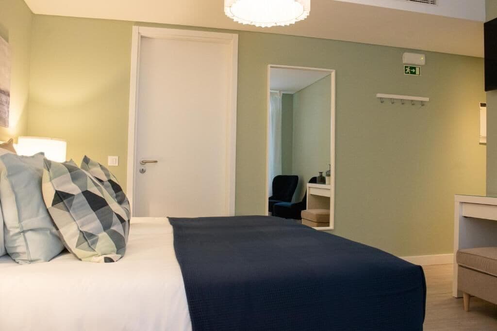 A hotel room with a bed, pillows, a chair, a desk, and a mirror.
