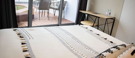 Habitación de hotel con una cama grande, vistas a un balcón exterior con una mesa y sillas, y un pequeño escritorio con botellas de agua.