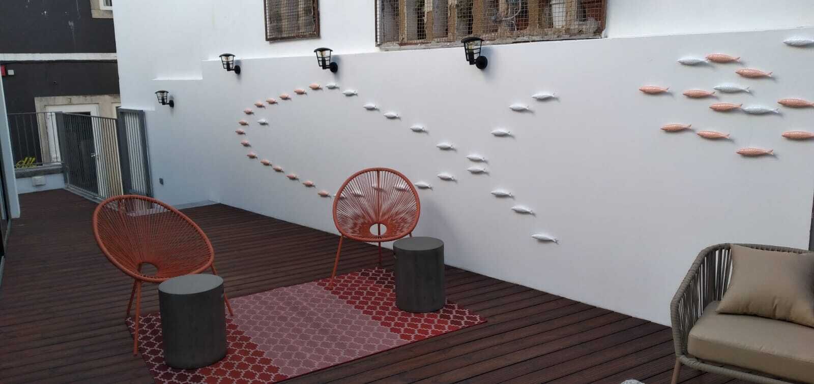 Un espace extérieur moderne, aménagé avec deux chaises orange, un tapis rouge à motifs et un mur décoré de motifs représentant des poissons.