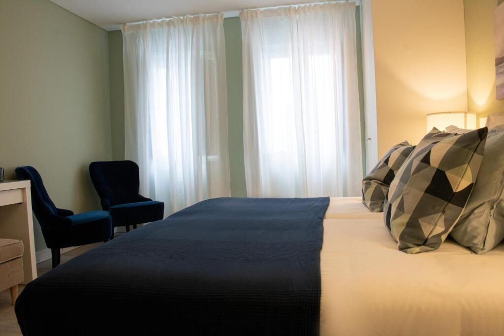 Habitación de hotel con cama, dos sillas, escritorio y ventana con cortinas.