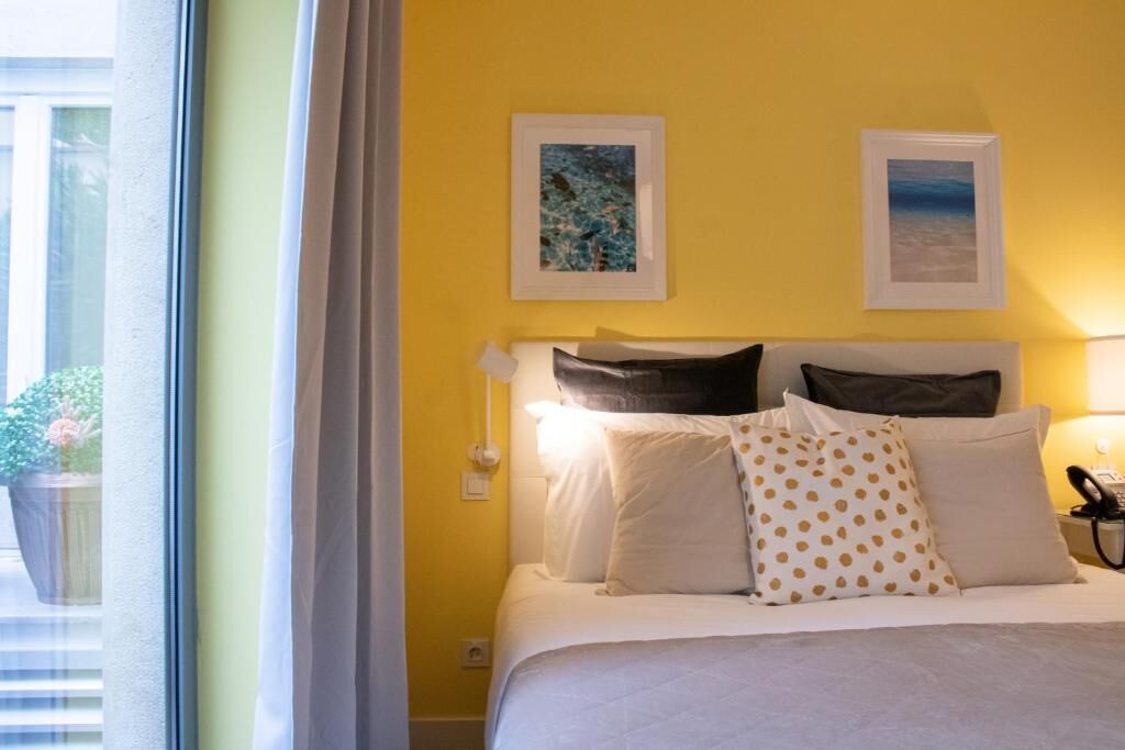 A hotel room with a bed, two framed pictures on the wall, and a window with curtains.