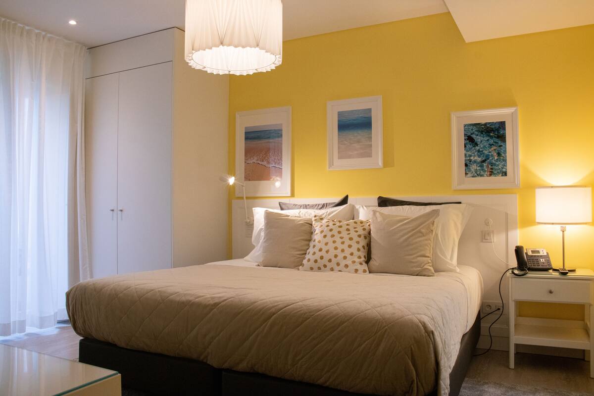 A bedroom with a bed, bedside table, lamp, and artwork on the wall.
