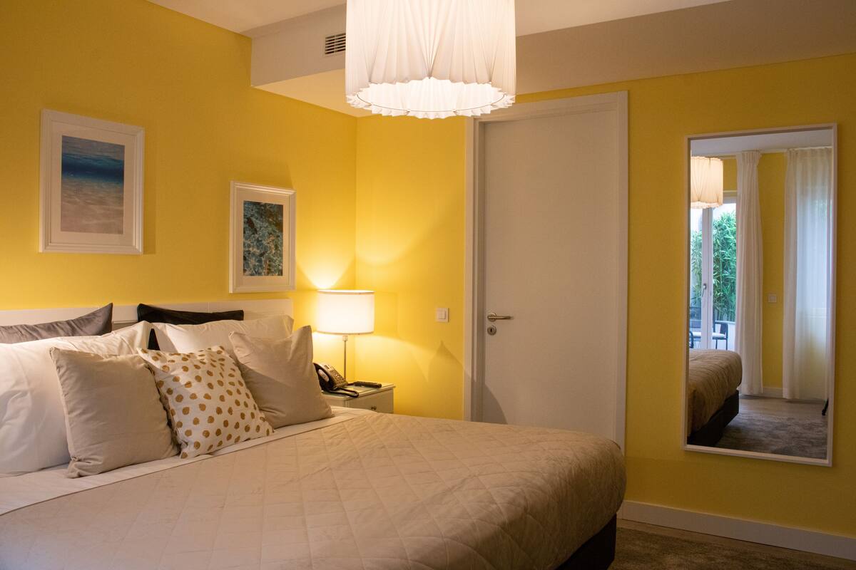 A bedroom with a bed, bedside table, lamp, and a mirror on the wall.