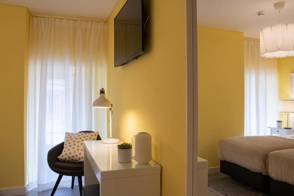 A hotel room with a bed, a desk with a lamp, a chair, and a TV mounted on the wall.