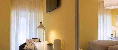 A hotel room with a bed, a desk with a lamp, a chair, and a TV mounted on the wall.