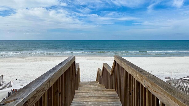Una passerella in legno che conduce a una spiaggia sotto un cielo sereno e un mare calmo.