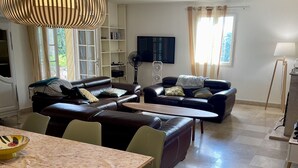 A living room with a sofa, a dining table, and a TV. - Magnificent villa in the heart of the Var for a superb vacation. (La Verdiere)
