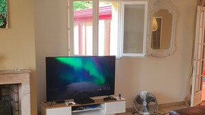 A living room with a flat-screen TV, a fireplace, a sofa, a wooden coffee table, and a fan. - Magnificent villa in the heart of the Var for a superb vacation. (La Verdiere)