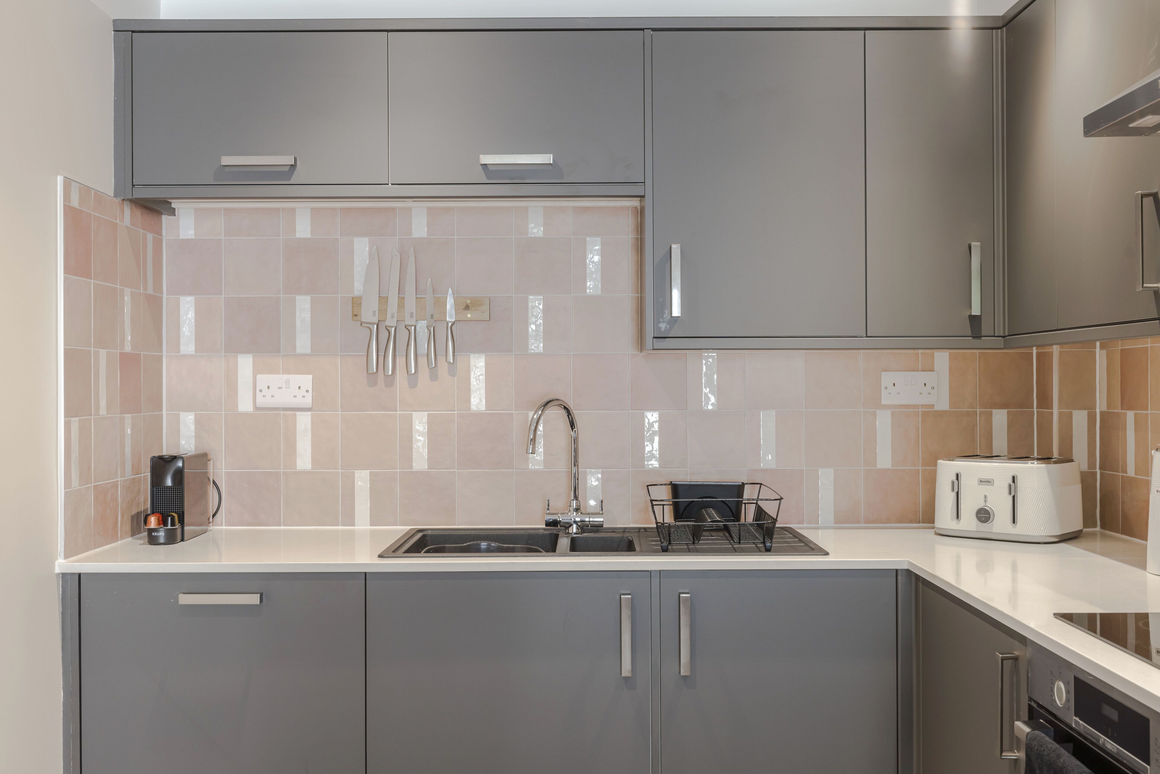 A modern kitchen with grey cabinets, a stainless steel sink, and a toaster on the countertop.