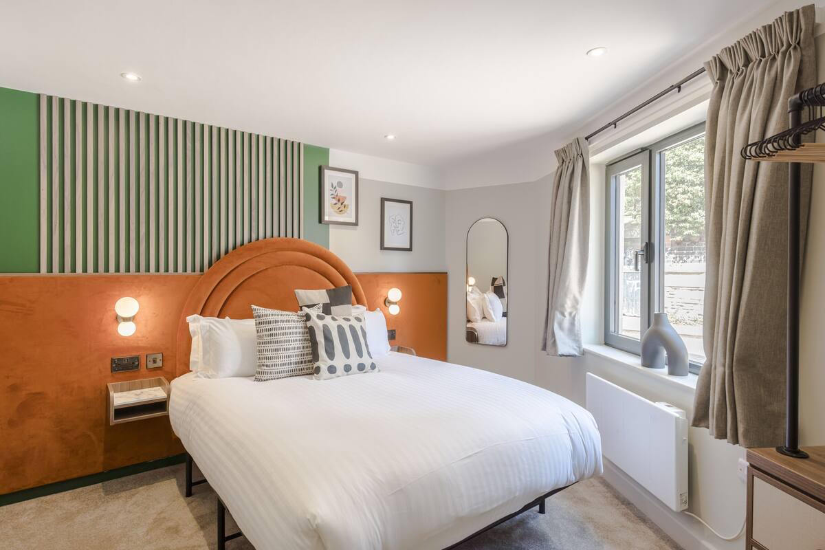 A neatly arranged bedroom with a bed, bedside tables, a mirror, and a window with curtains.
