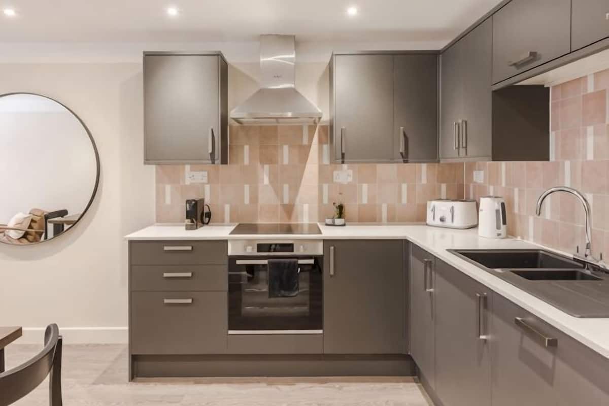 A modern kitchen with grey cabinets, a built-in oven, a sink, and a round mirror on the wall.