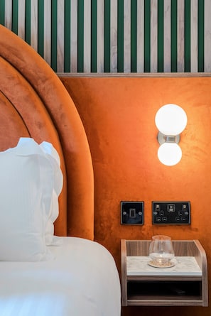 A hotel room with a curved orange headboard, a white pillow, a bedside table with a glass vase, and a wall-mounted light fixture. - Arabica House - YourApartment (Bristol)