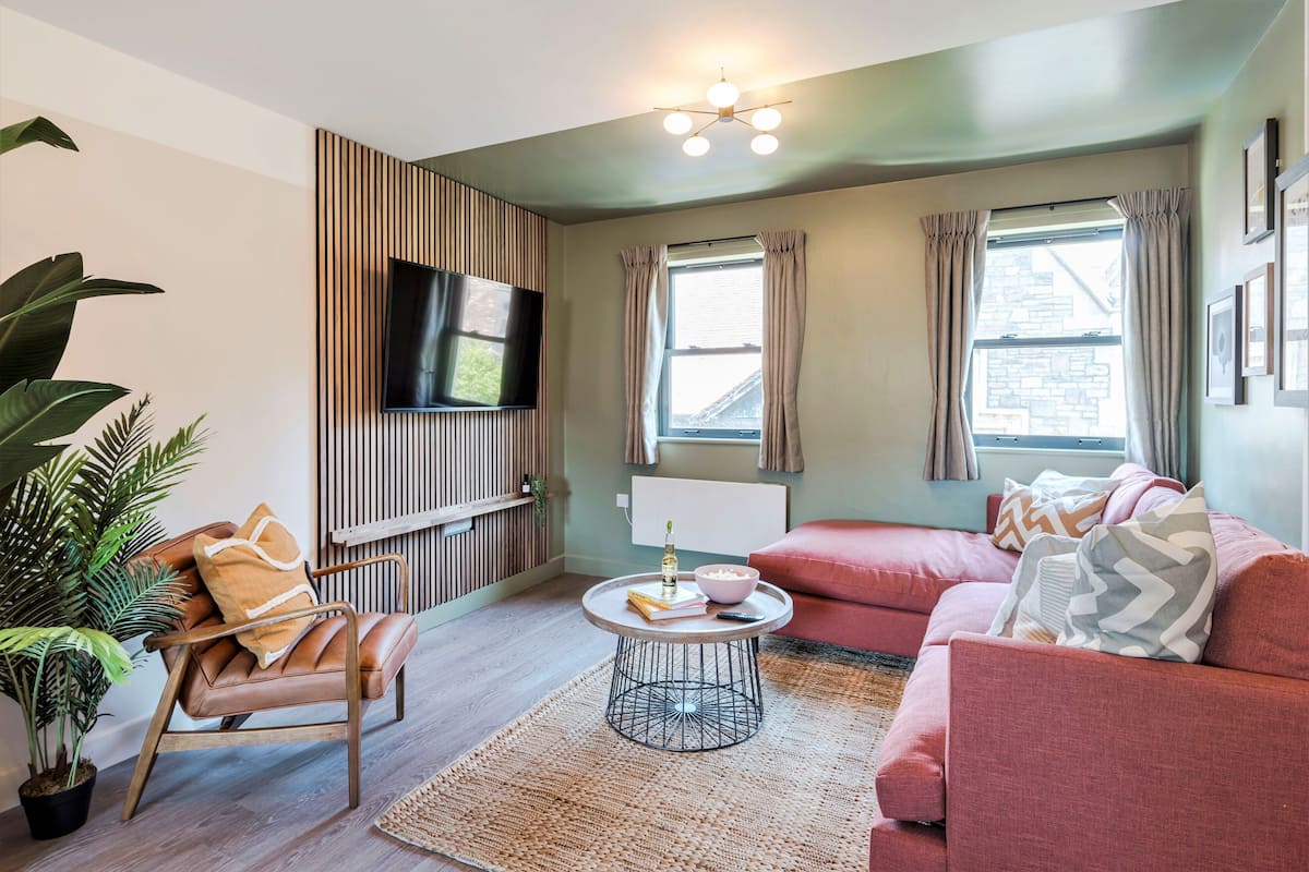A modern living room with a leather chair, a red sofa, a round coffee table, and a flat-screen TV mounted on the wall.