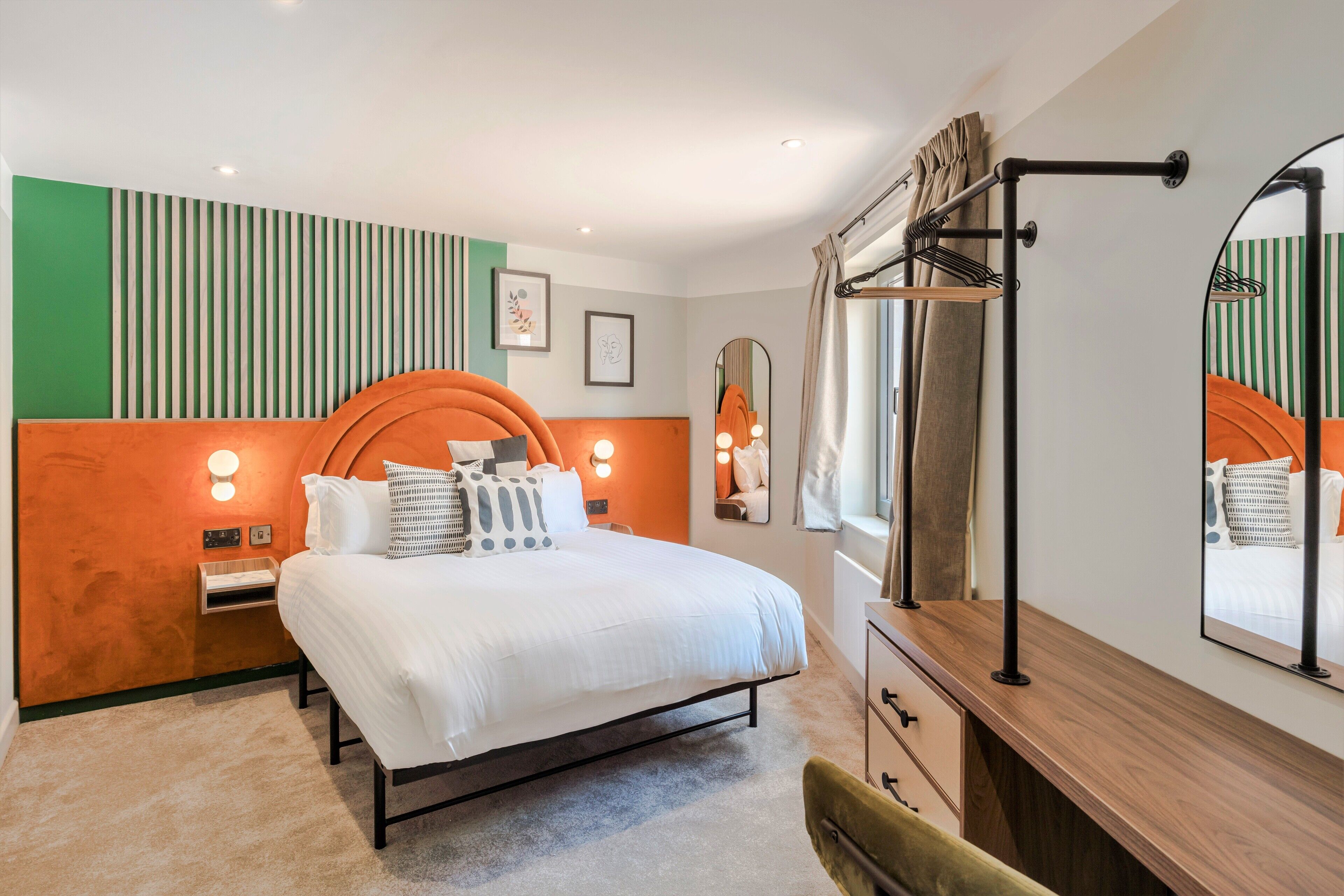 Un dormitorio moderno con cama, mesitas de noche, cómoda, espejo y ventana con cortinas.