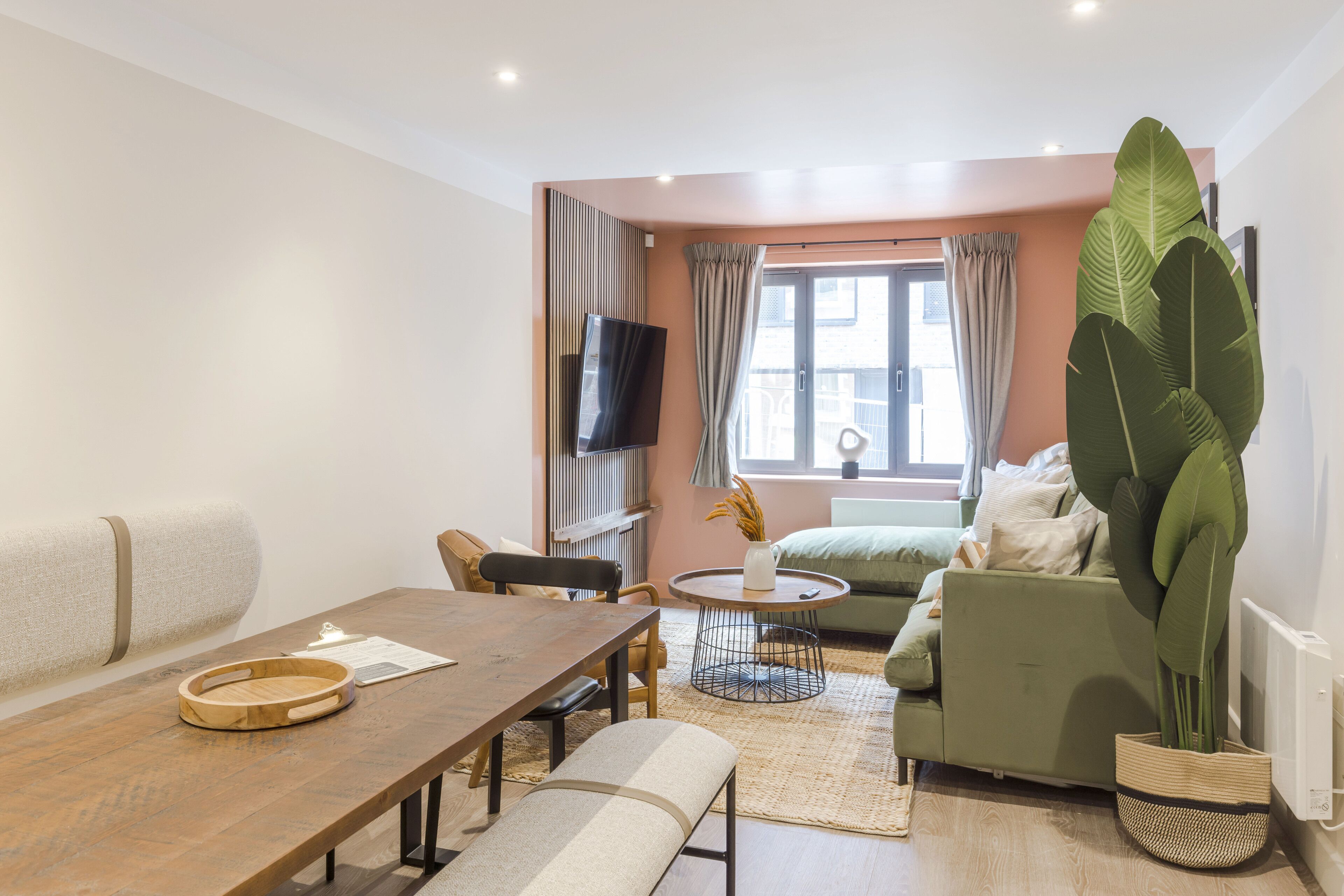 En moderne stue med et træbord, en grøn sofa og en stor plante.