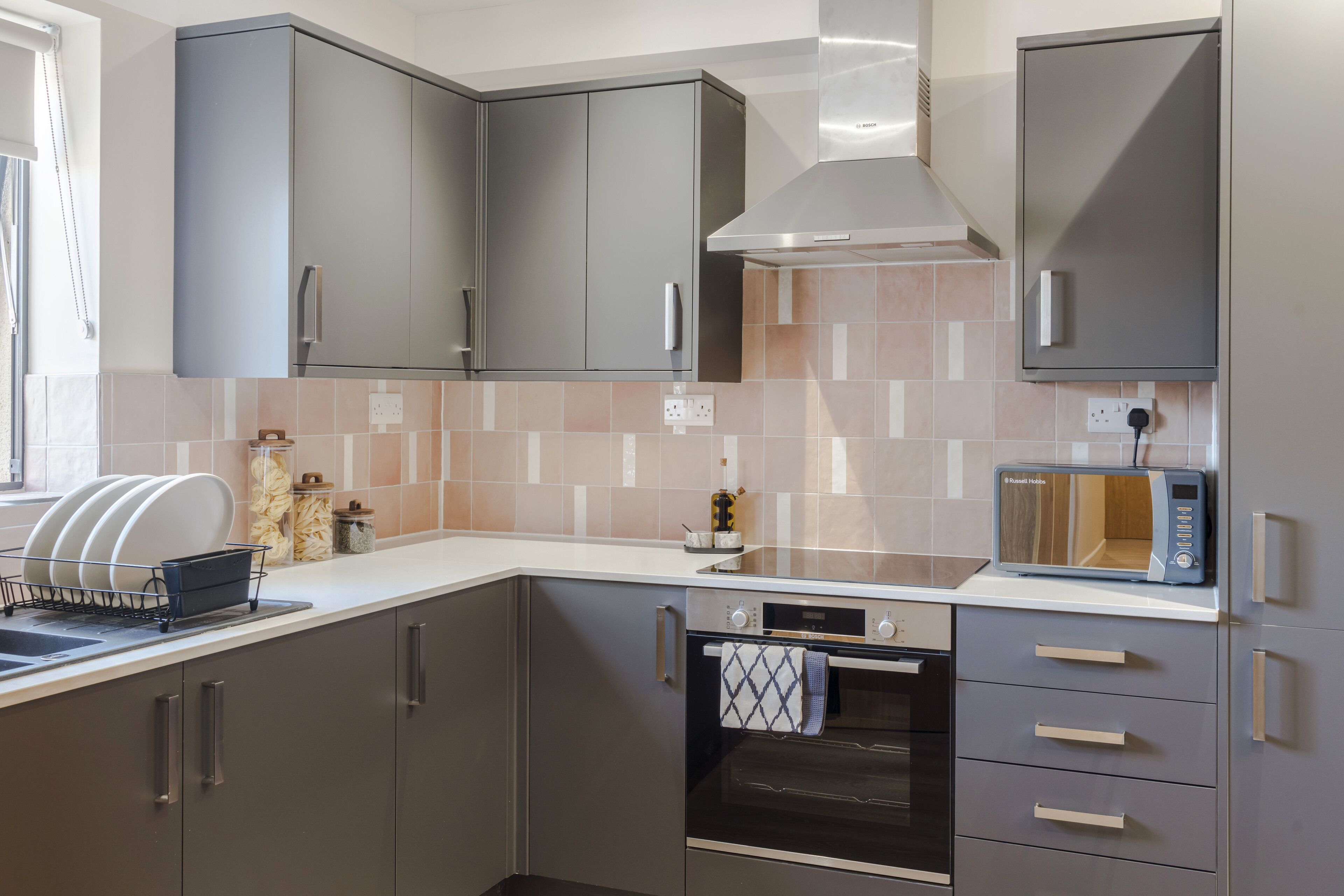 A modern kitchen with grey cabinets, a built-in oven, a microwave, and a dish rack.