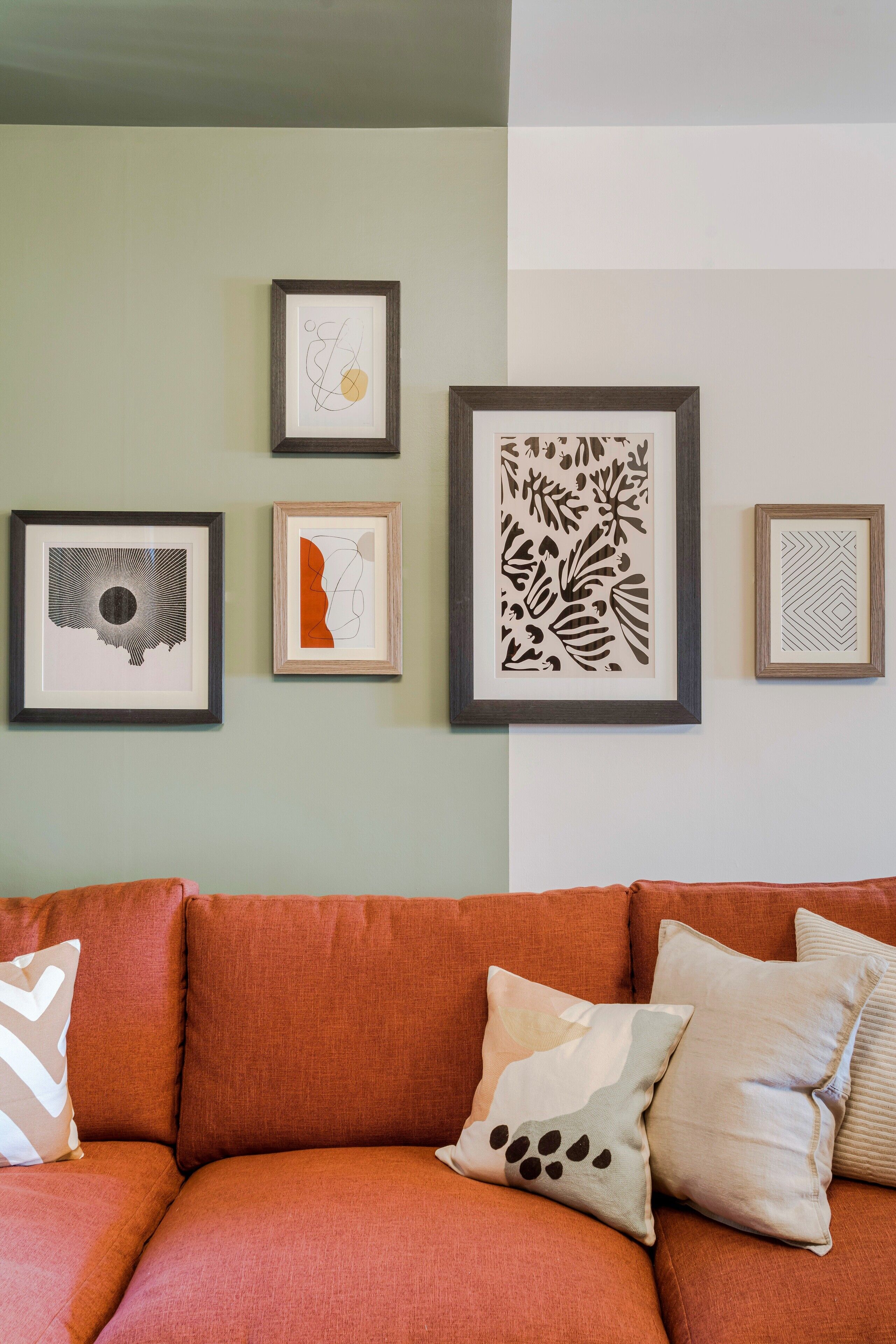 Ein Wohnzimmer mit einem braunen Sofa, vier gerahmten Kunstwerken an der Wand und drei Kissen.