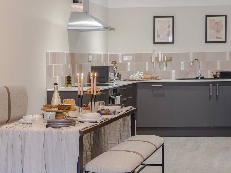 A modern kitchen with grey cabinets, a stainless steel range hood, and a dining area with a table set for four.