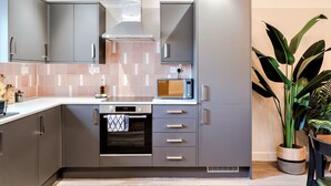 Een moderne keuken met grijze kastjes, een inbouwoven, een magnetron en een grote potplant.