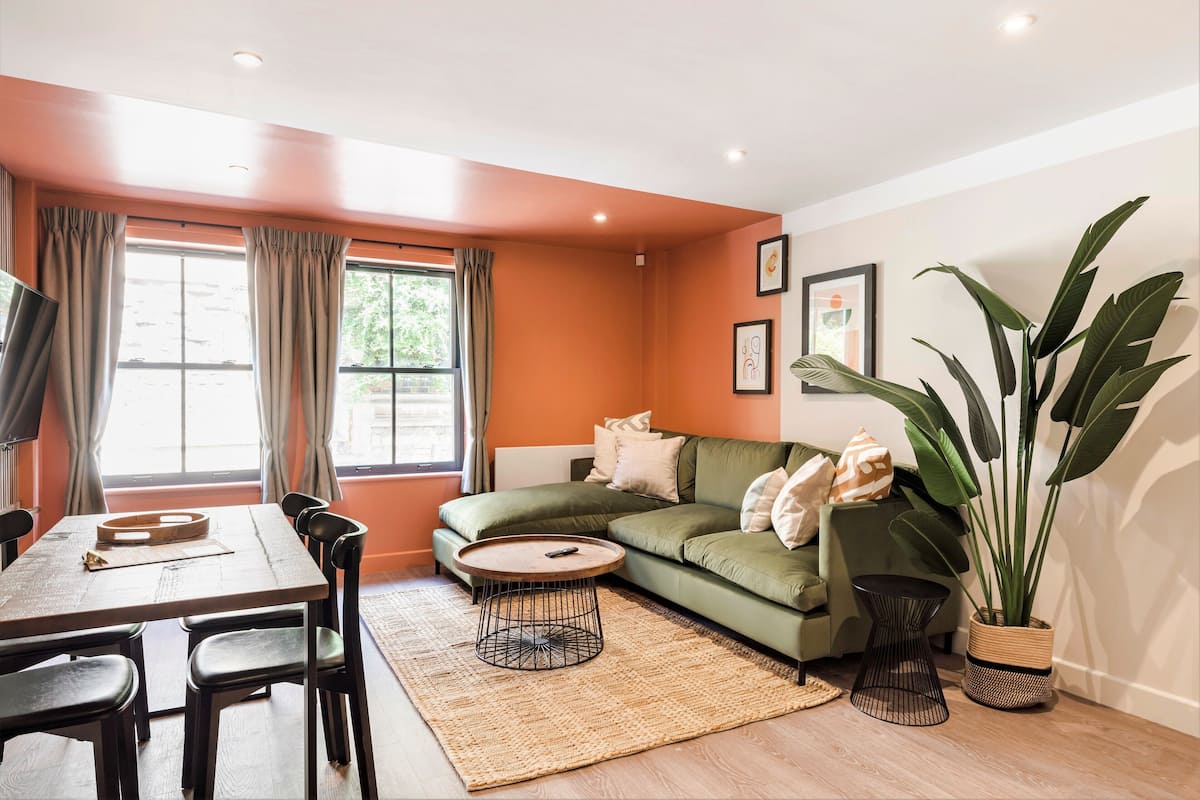 A living room with a green sofa, a dining table with chairs, a coffee table, and a large plant.