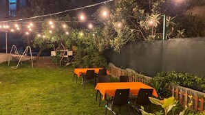 An outdoor dining area with tables and chairs, string lights, and a grassy lawn.