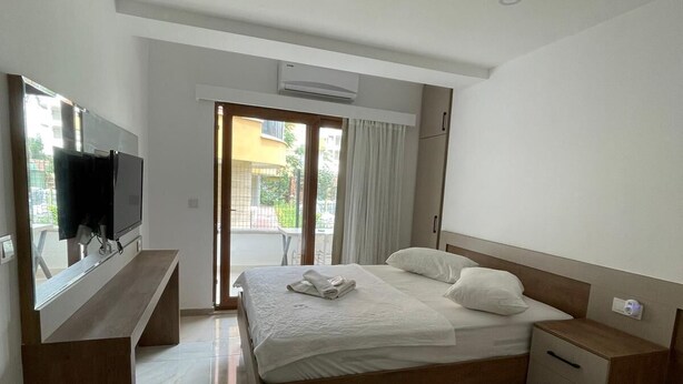 A modern hotel room with a bed, bedside tables, a TV, and a view of the outside.
