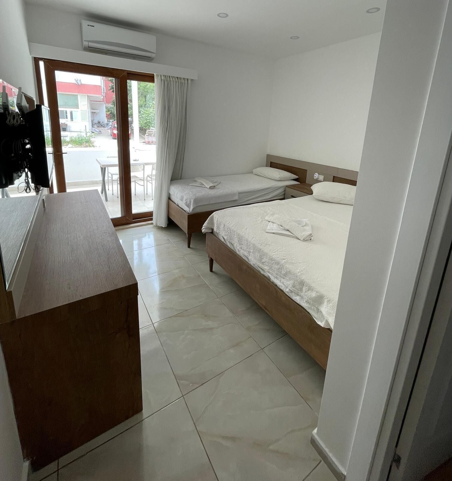 A hotel room with two beds, a desk, and a sliding glass door to the outside.