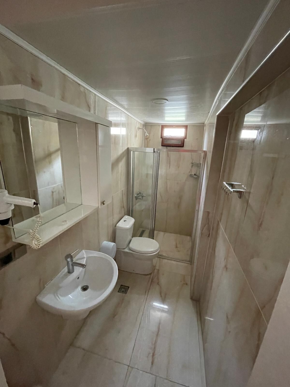 A compact bathroom with a sink, toilet, and glass shower enclosure.