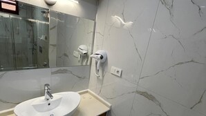 A modern bathroom with a marble vanity, a large mirror, and a glass shower enclosure.