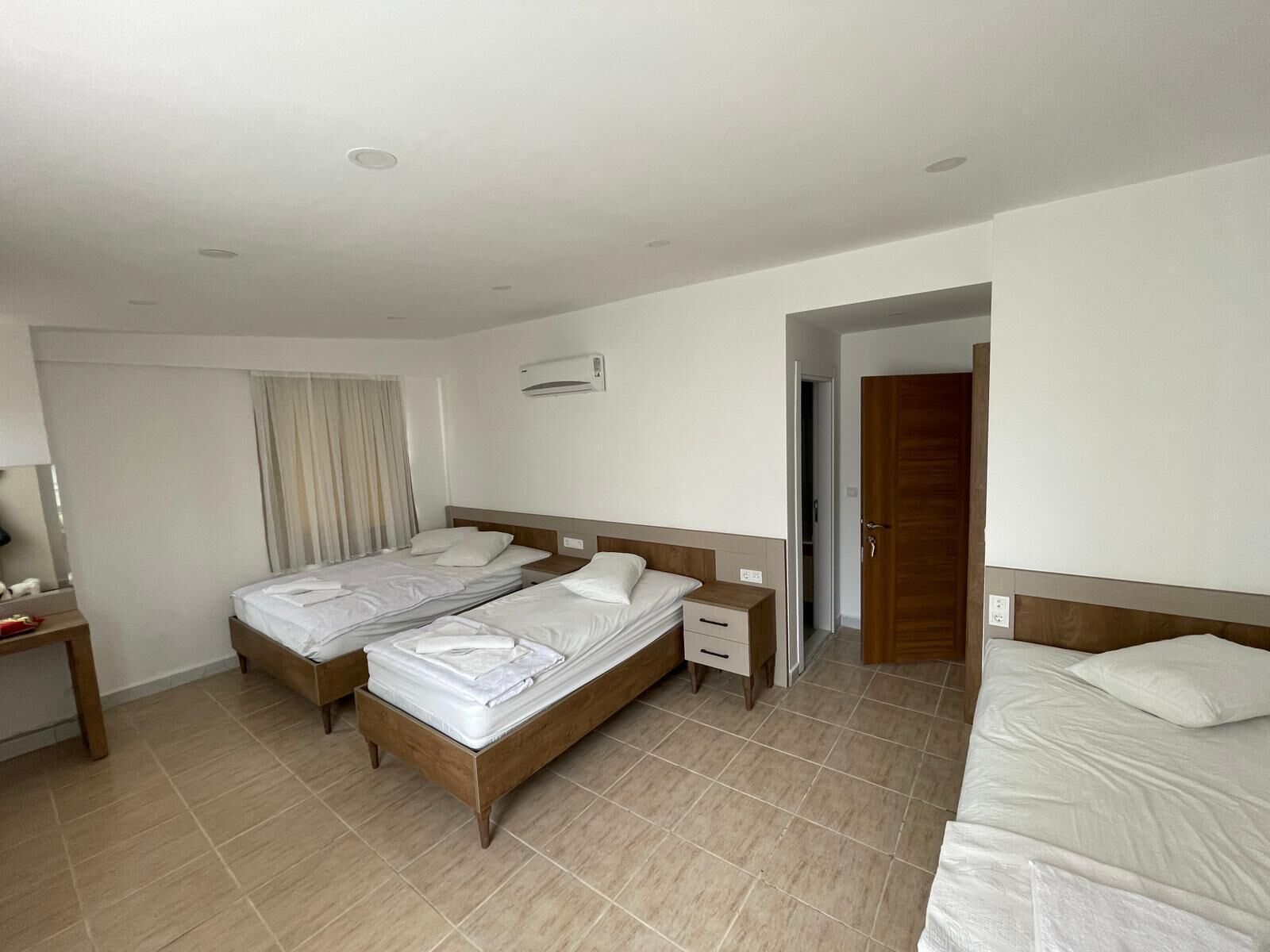 A hotel room with two single beds, a wooden nightstand, a bedside table, and a built-in air conditioning unit.