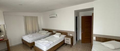 A hotel room with two single beds, a wooden nightstand, a bedside table, and a built-in air conditioning unit.